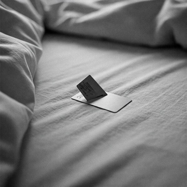 A hotel keycard lies open on a white bed, symbolizing silent consent and setup for CMNF ritual and public use erotica.